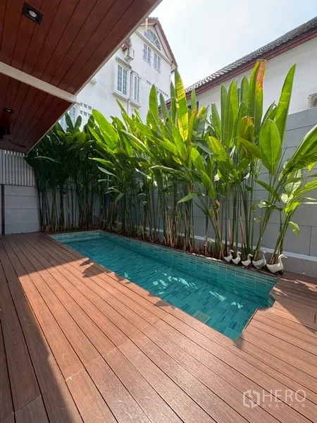 บ้านแฝด for rent in Watthana, Bangkok - มุมมองอีกด้านของสระว่ายน้ำข้างแนวต้นไม้และพื้นไม้ระเบียง