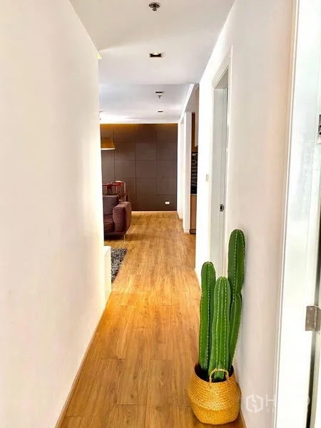 Condominium for rent in Khlong Toei, Bangkok - Hallway with wooden floor, white walls and a potted cactus leading to the lounge.