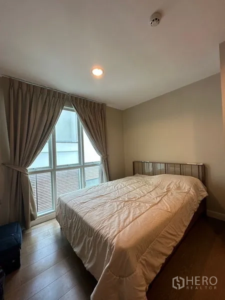 Condominium for rent in Khlong Toei, Bangkok - Bedroom with large window, curtains and double bed on wood flooring.