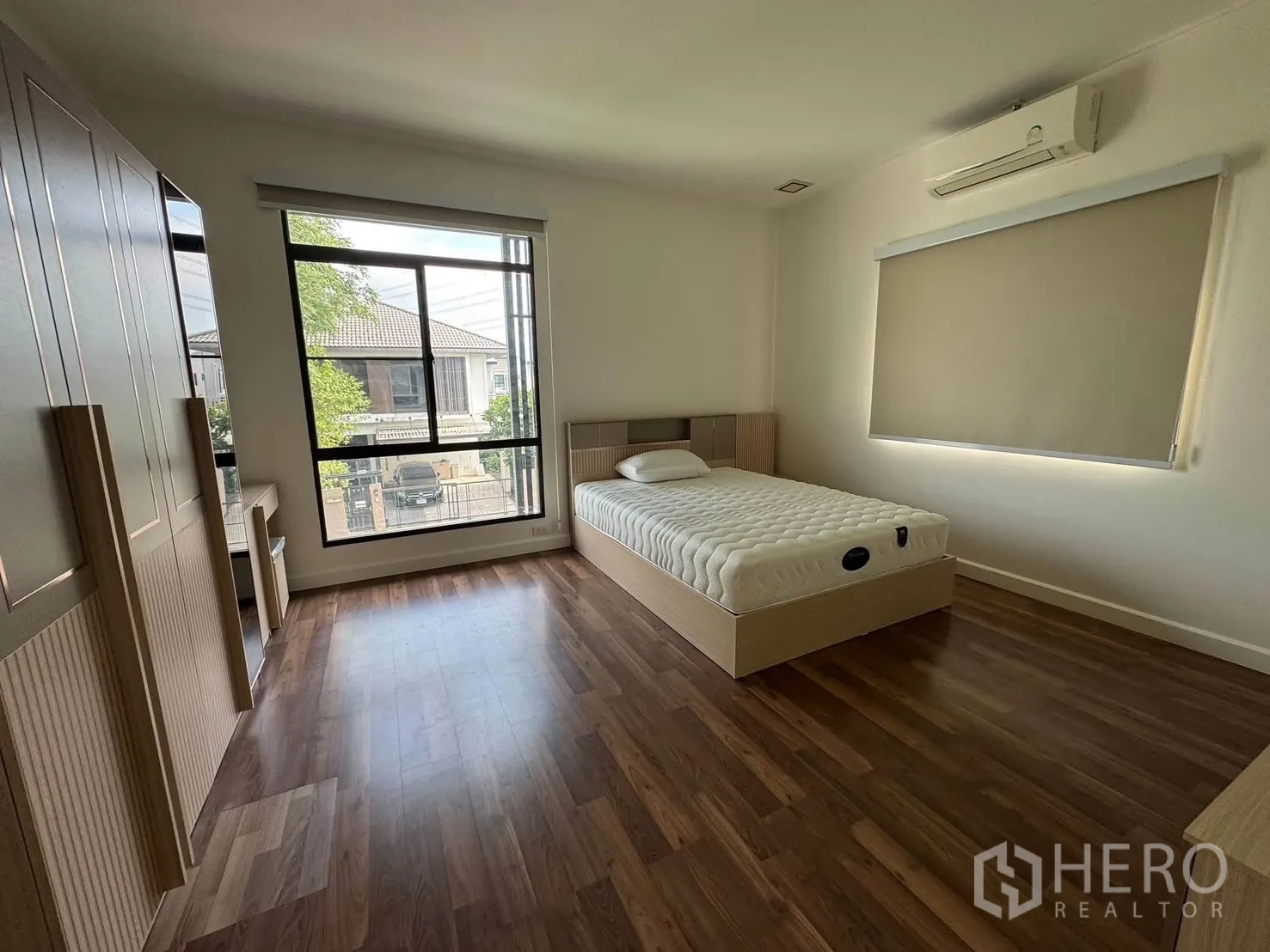 Detached House for rent in Prawet, Bangkok - Spacious bedroom with bed, wardrobe set, desk, wood floors, and a large window.
