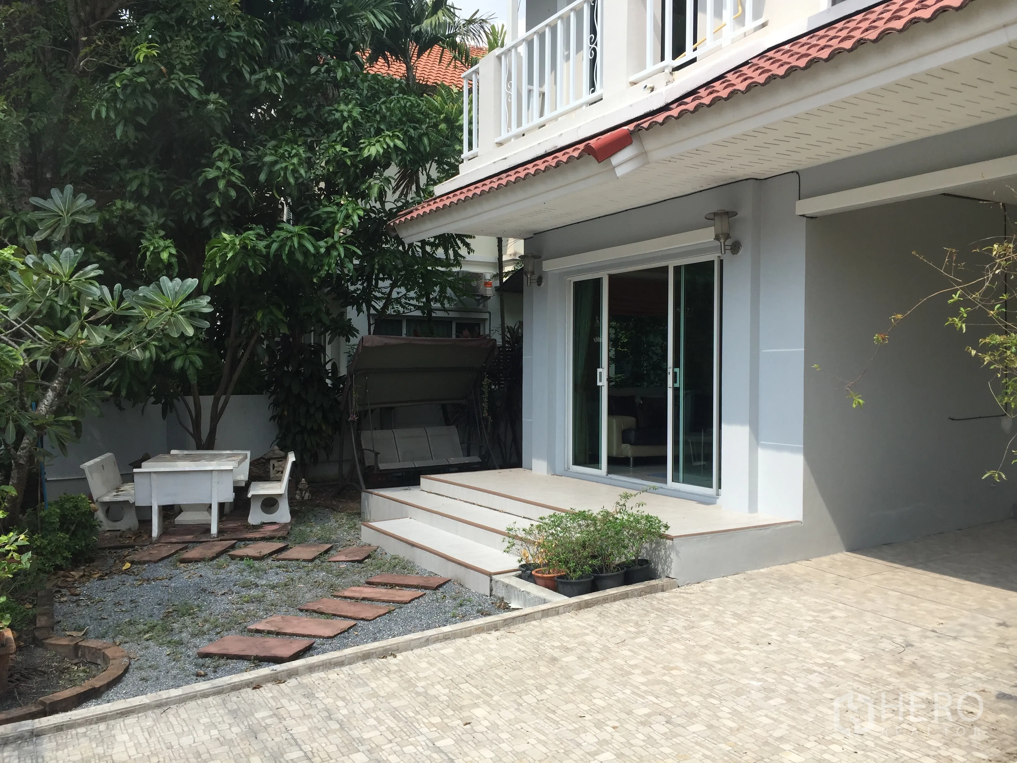 Detached House for sale in Lat Krabang, Bangkok - Front patio with sliding glass doors opening to a small garden, swing seat and outdoor table.