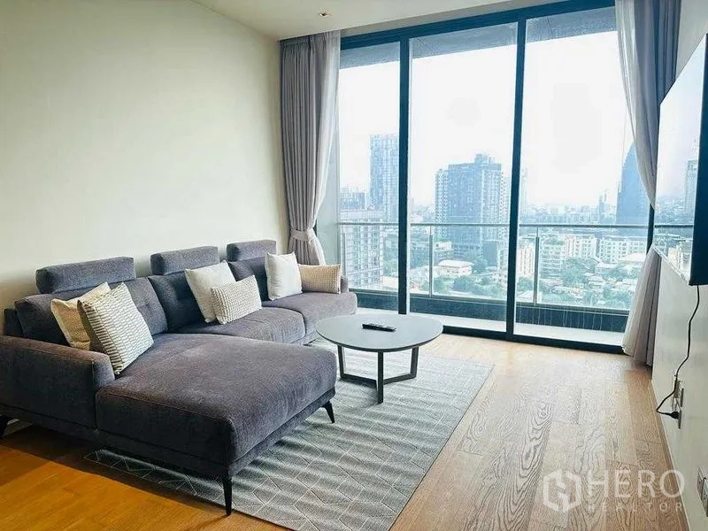 Condominium for rent in Khlong Toei, Bangkok - Lounge area with large sectional sofa and full-height glass doors to the balcony.