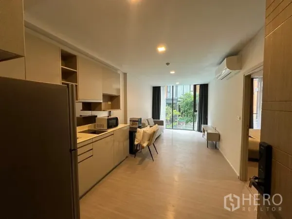 Condominium for rent in Khlong Toei, Bangkok - Open-plan living space from entrance showing kitchenette, dining area, and large sliding doors to garden views.
