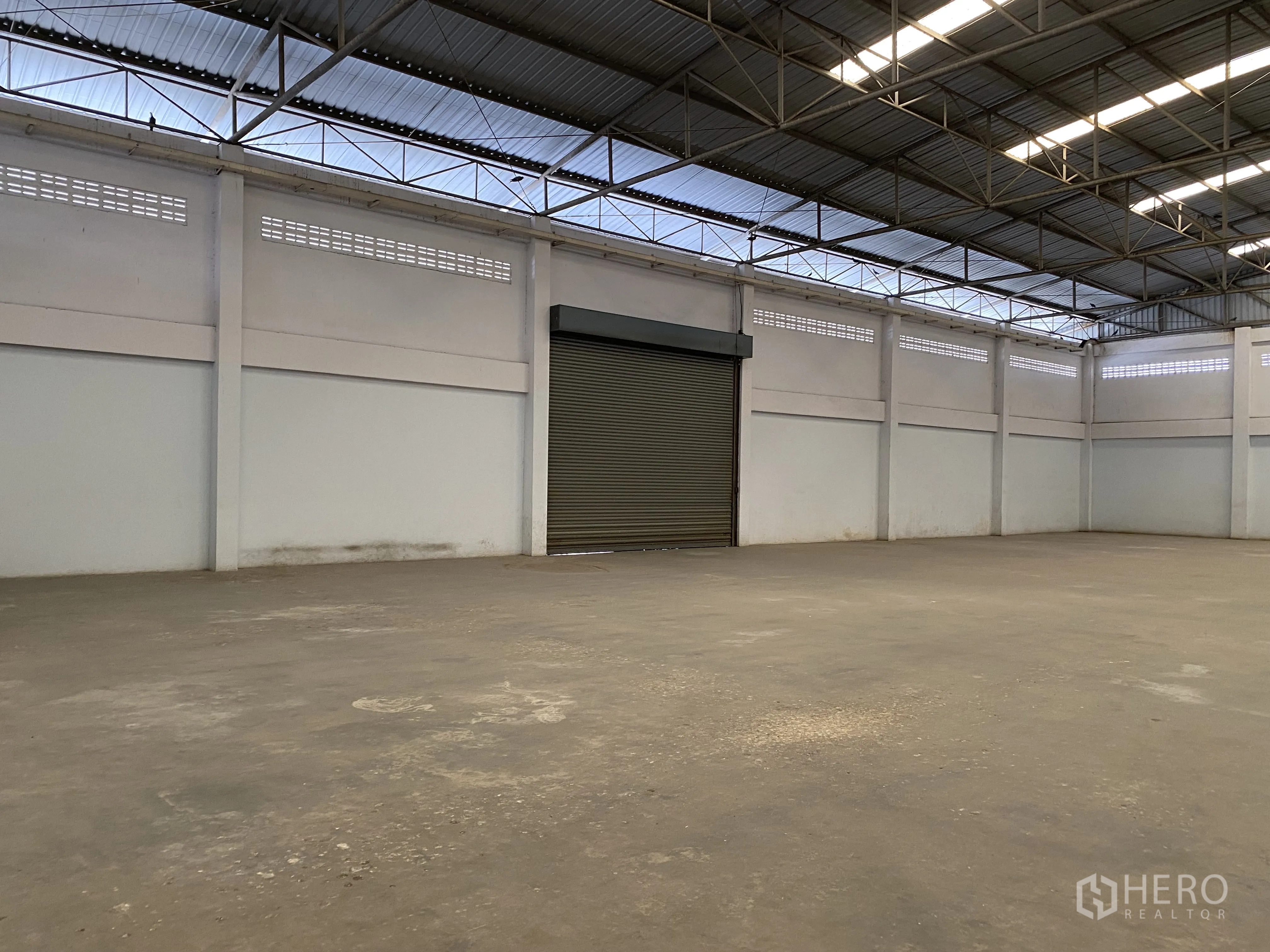 Factory for sale in Khlong Luang, Pathum Thani - Warehouse corner with a wide roller shutter door.