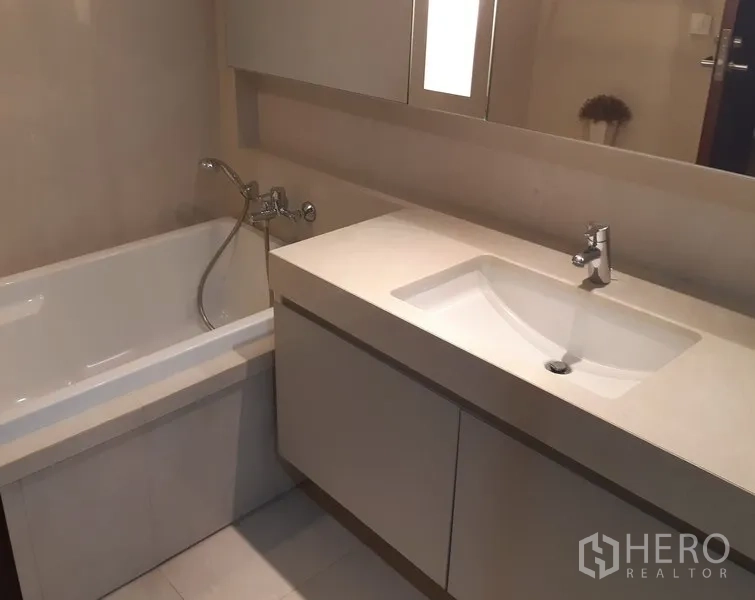 公寓 出租在Watthana, Bangkok - 浴室设有一体式台盆柜与镜柜，旁边为浴缸。