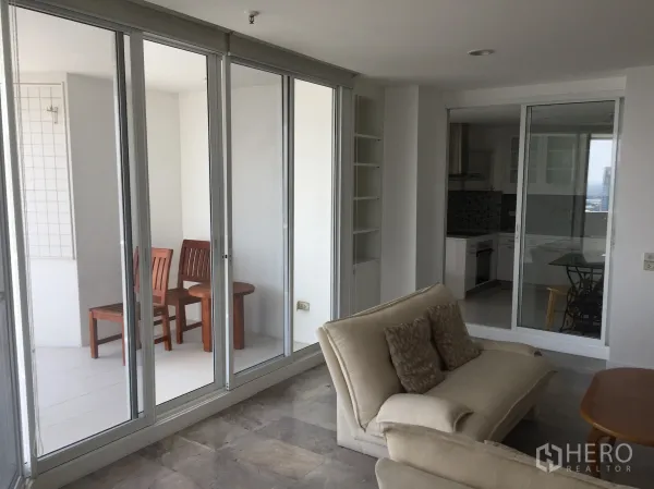 公寓 出租在Watthana, Bangkok - 客厅连接玻璃封闭阳台座位区，与独立厨房相邻。