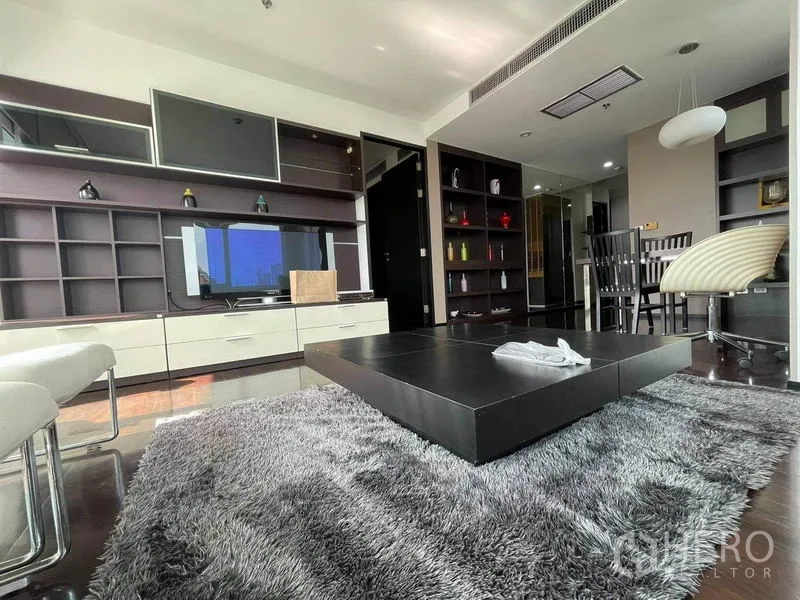 公寓 出租或出售在Watthana, Bangkok - 客厅设嵌入式收纳与电视墙，矮方茶几与长绒地毯，旁接用餐区