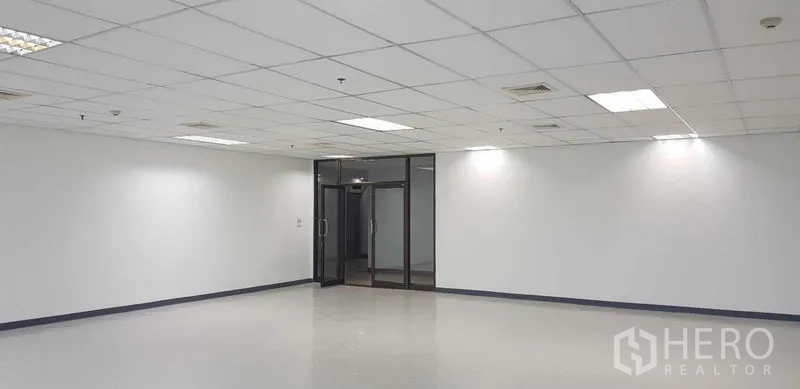Office Space for rent in Khlong Toei, Bangkok - Interior of vacant office space showing suspended grid ceiling, bright lighting, and a glass double-door entrance.