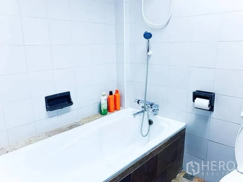 Home Office for rent in Khlong Toei, Bangkok - White tiled bathroom with bathtub, handheld shower and toiletries.