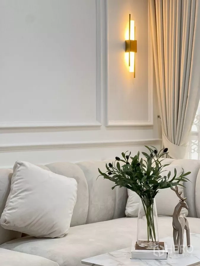 Detached House for rent in Huai Khwang, Bangkok - Close-up of wall moulding and brass sconce above a plush cream sofa with decor.