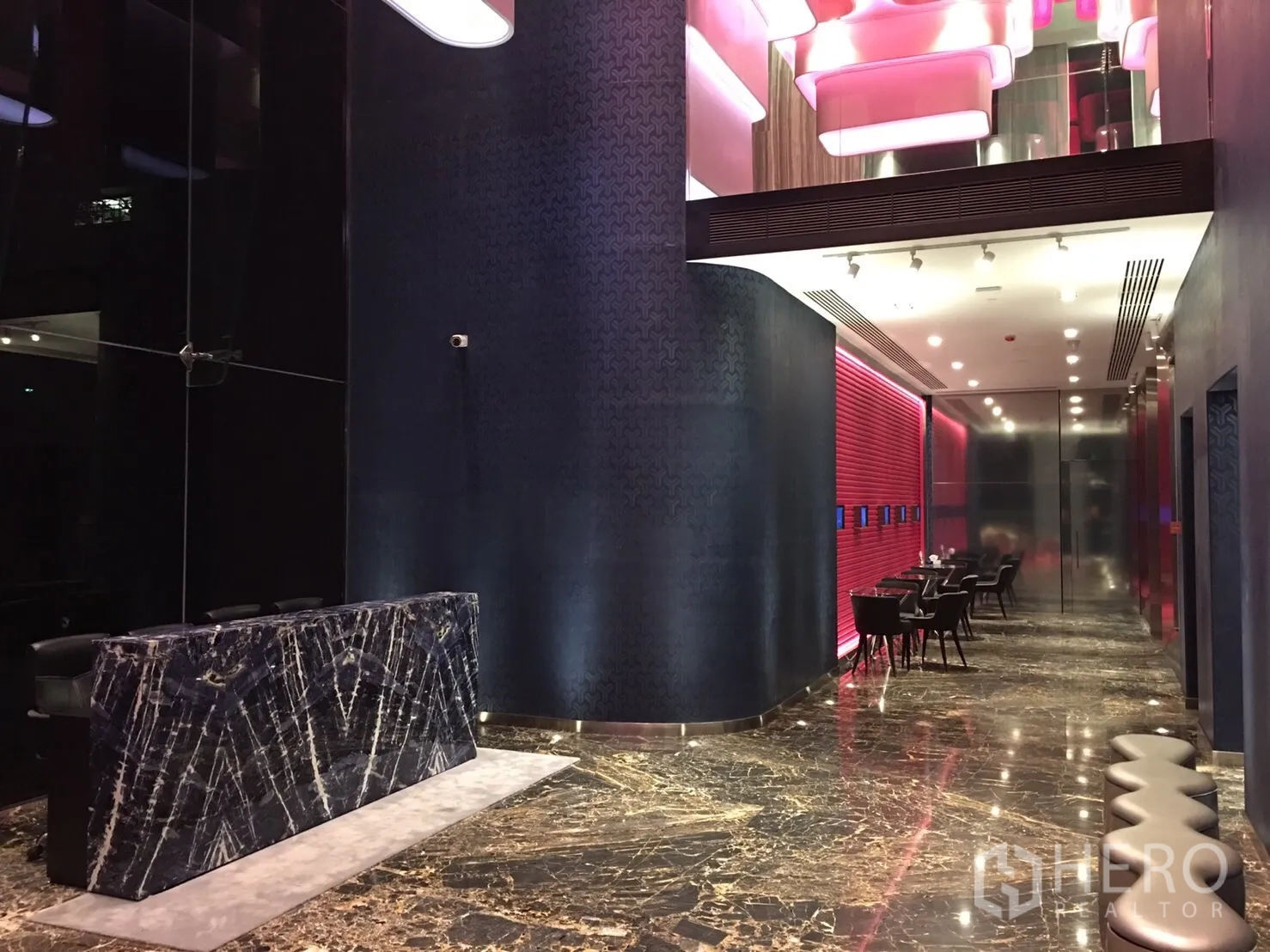 公寓 出租在Watthana, Bangkok - 公寓大堂，铺设大理石地面，深色石材前台，粉色天花灯与休息区。