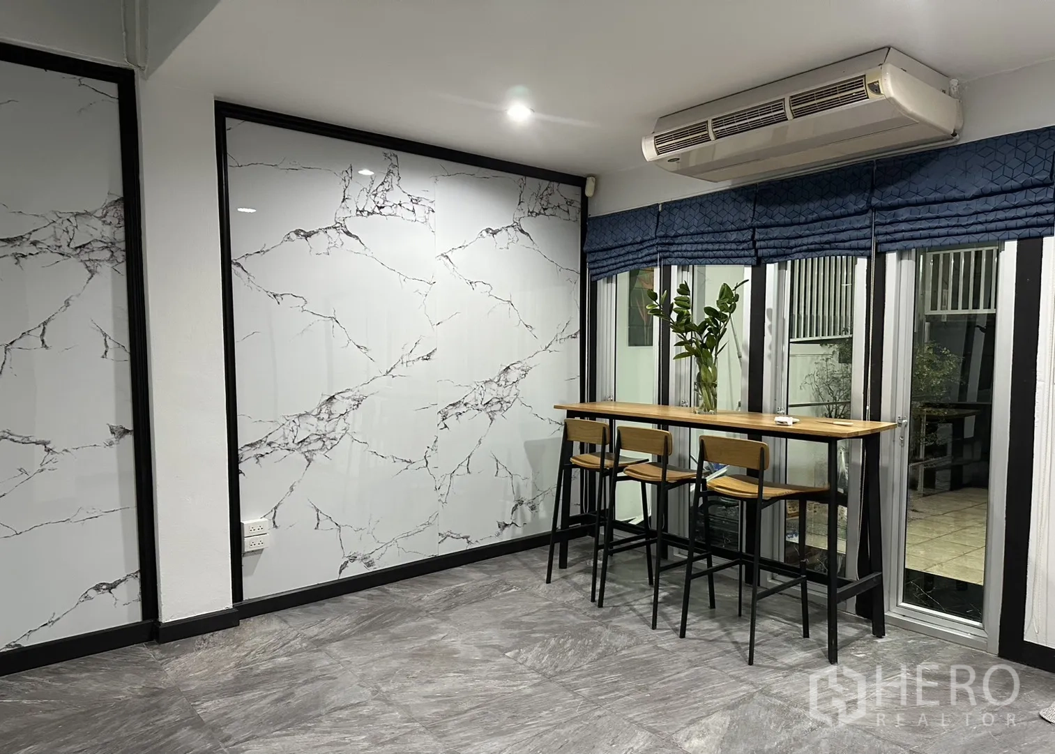 Home Office for rent in Khlong Toei, Bangkok - Dining corner with a high bar table, three stools, and wide windows beneath an AC unit.