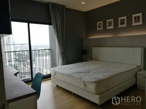 Condominium for rent in Watthana, Bangkok - Bright master bedroom with upholstered bed, floor-to-ceiling windows and a balcony overlooking the city.