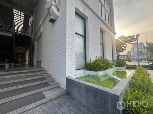零售空间 出租在Khlong Toei, Bangkok - 建筑转角配景观水池、台阶与城市黄昏景色。