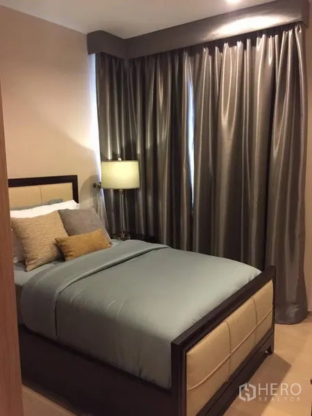 Condominium for rent in Watthana, Bangkok - Cozy bedroom with double bed, bedside lamp, layered pillows and blackout curtains.