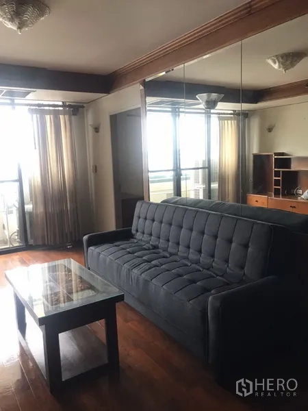 公寓 出租在Watthana, Bangkok - 明亮客厅，深灰色沙发、玻璃茶几、木地板与阳台推拉门。