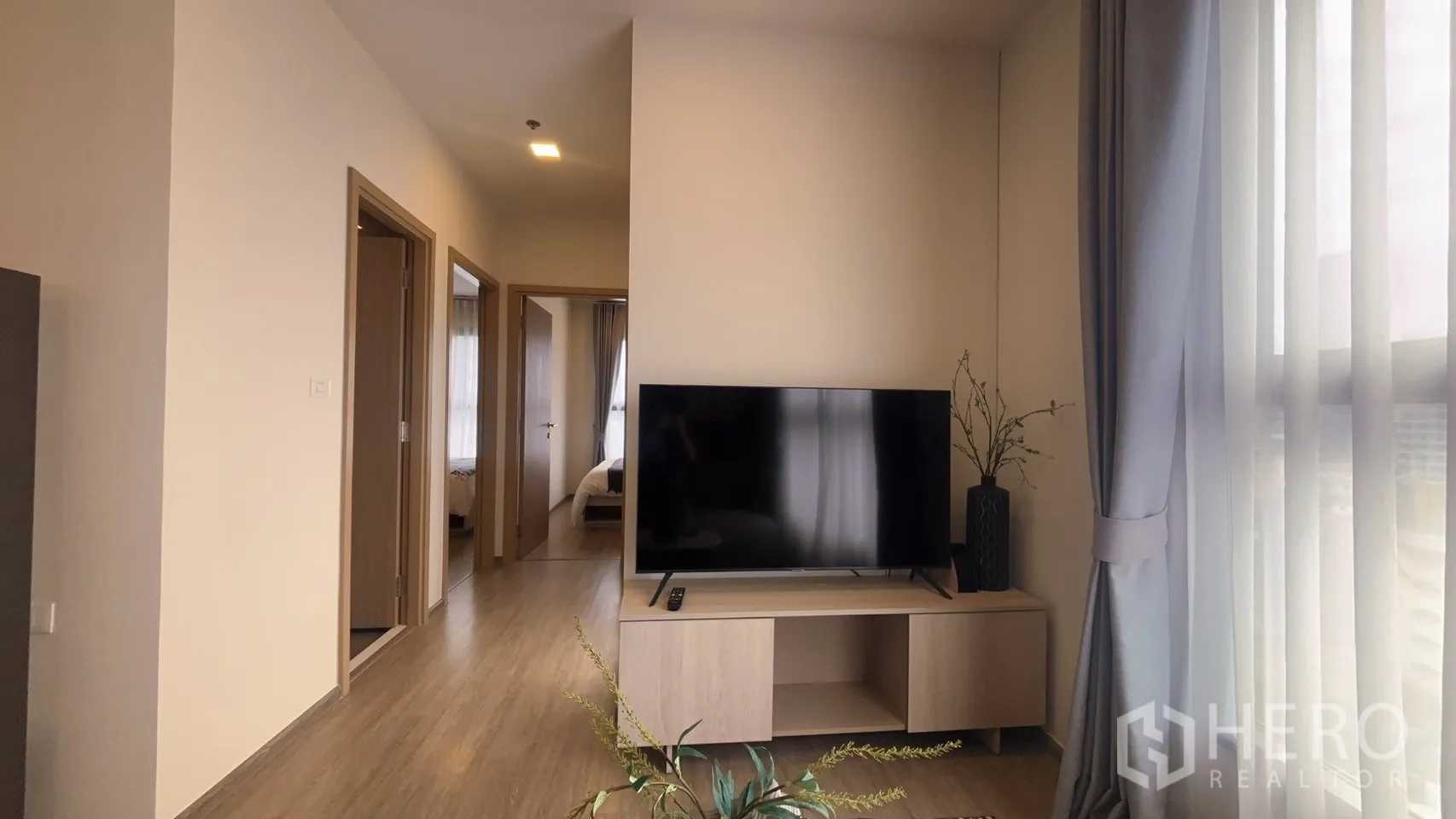 公寓 for rent in Watthana, Bangkok - 客厅电视柜与通往卧室的走廊，大窗帘引入自然光。
