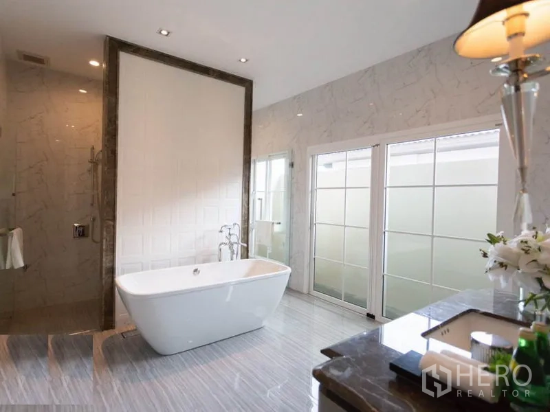 Detached House for rent in Mueang Samut Prakan, Samut Prakan - Luxurious bathroom featuring freestanding bathtub, glass shower, marble walls and large frosted windows.