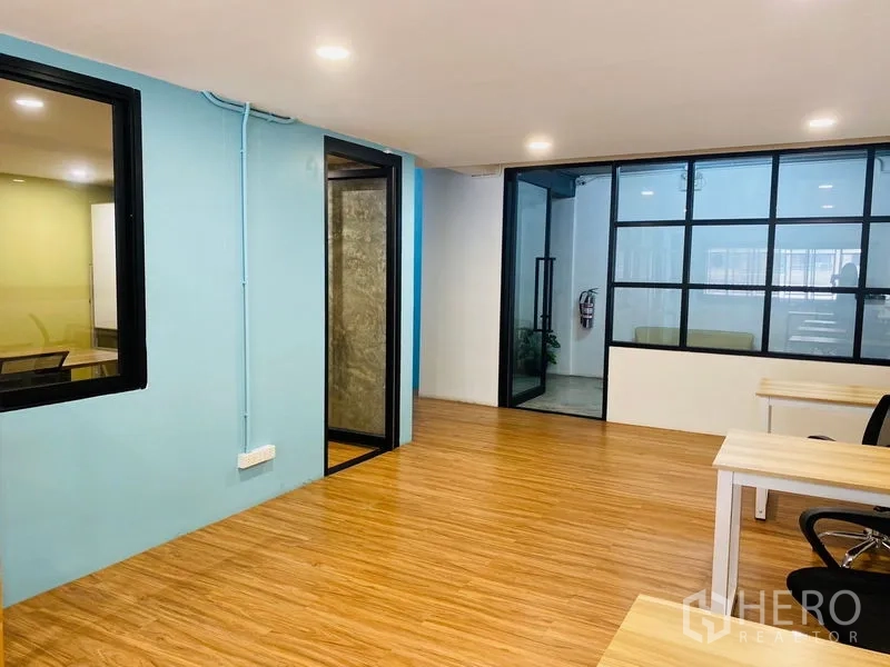 Office Space for rent in Bang Rak, Bangkok - Open-plan office with wood floors, blue accent wall and black-framed glass partitions.