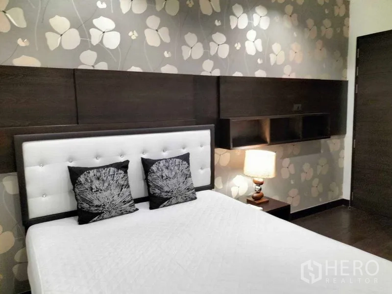 Condominium for rent in Ratchathewi, Bangkok - Second bedroom with floral wallpaper, tufted headboard and bedside lamp.