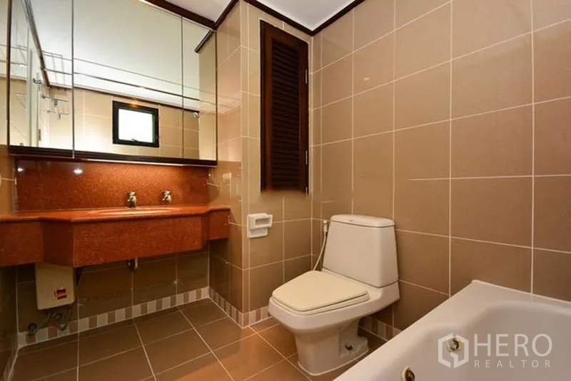 Apartment for rent in Khlong Toei, Bangkok - Second bathroom with double sinks, large mirror, bathtub and neutral ceramic tiles.