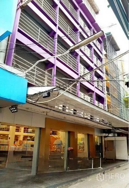 店屋 出租在Pathum Wan, Bangkok - 曼谷帕吞旺多层紫色商铺外立面，底层宽幅玻璃门面与金属百叶遮阳。