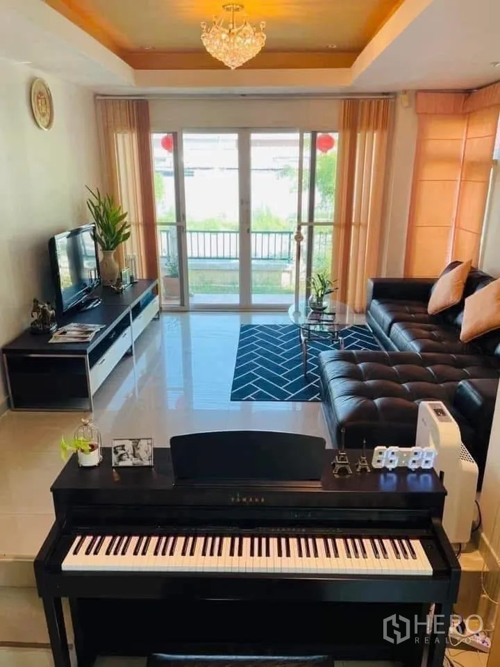 Detached House for rent or sale in Lam Luk Ka, Pathum Thani - Living area facing garden through wide sliding doors with piano and TV console.
