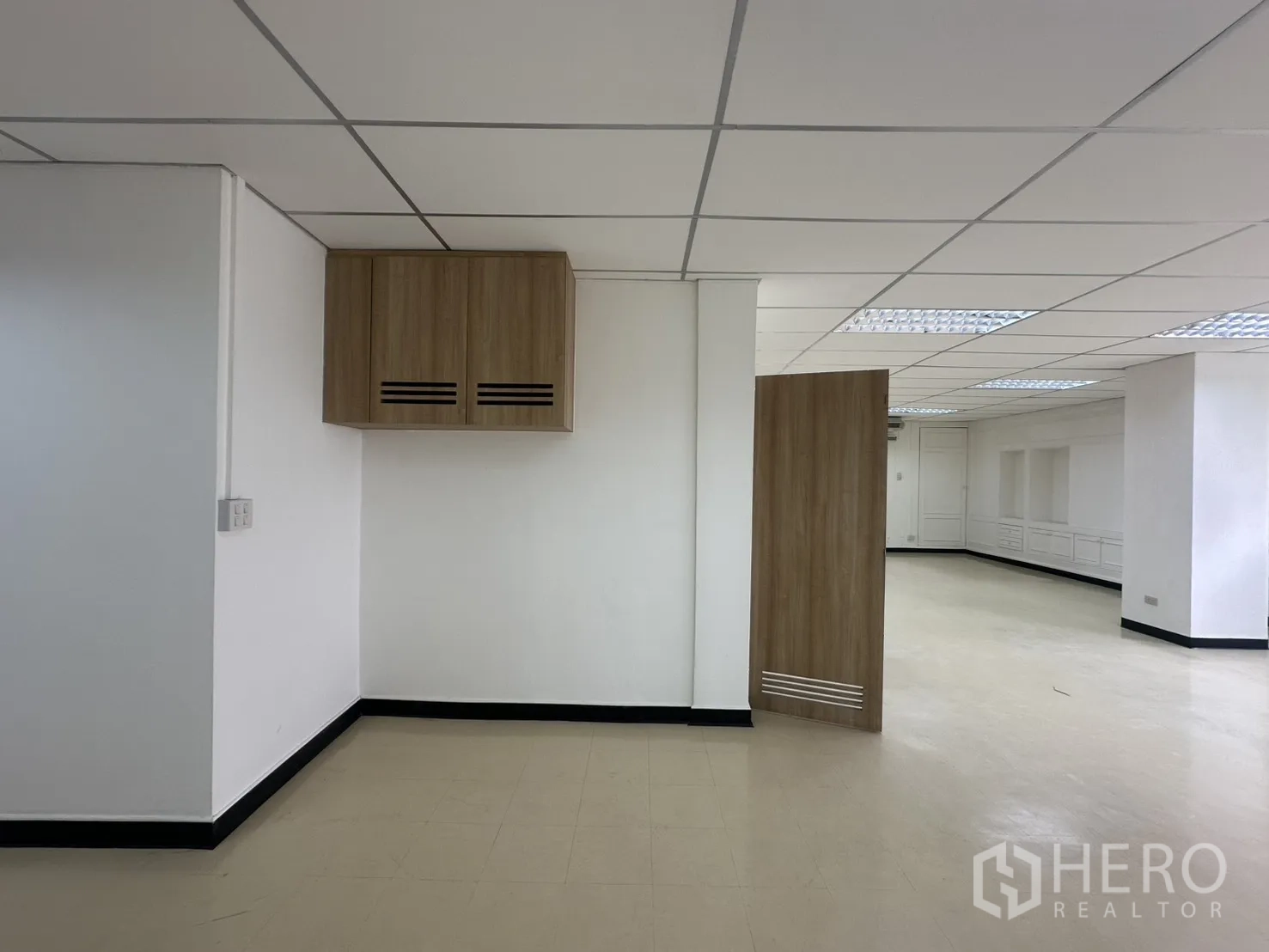 Office Space for rent in Pathum Wan, Bangkok - Corner of the office showing a wall-mounted storage cabinet, white walls, and an open area beyond a wooden door.