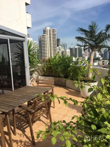 公寓 出租在Khlong Toei, Bangkok - 宽敞露台设户外餐桌椅，热带植物和全景城市景观。