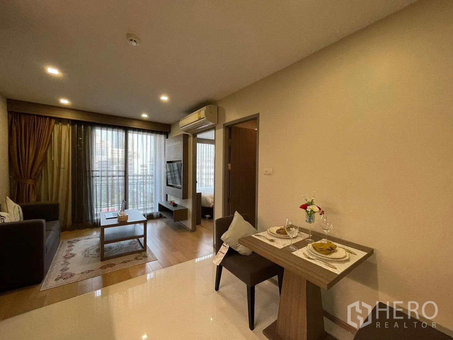 คอนโด for rent in Watthana, Bangkok - ห้องนั่งเล่นมีประตูกระจกออกระเบียง ทีวีติดผนัง และโต๊ะทานข้าวขนาดกะทัดรัดสำหรับสองคน