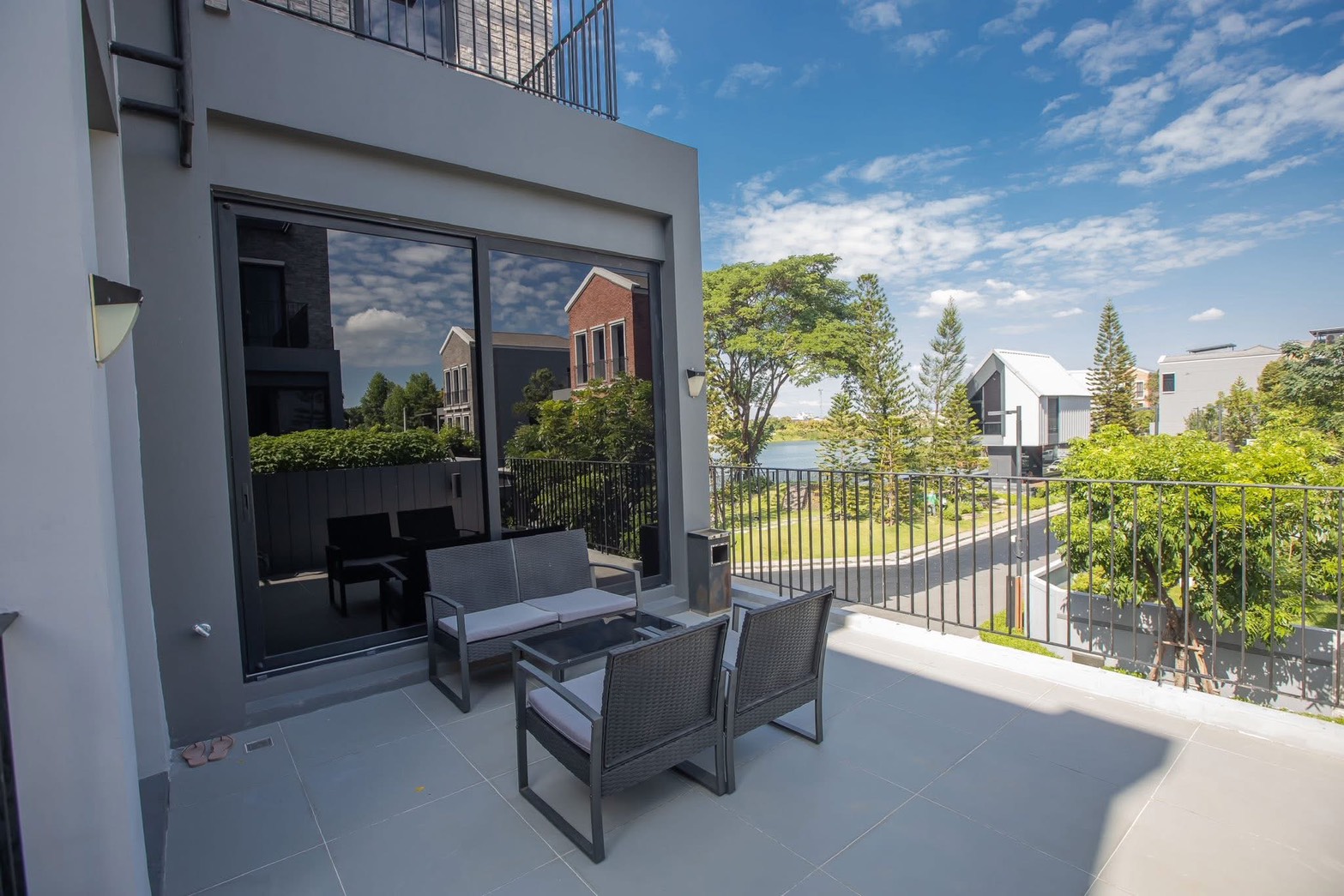 Detached House for rent in Lat Phrao, Bangkok - Sunny terrace with outdoor lounge set and railing overlooking trees and a community lake.