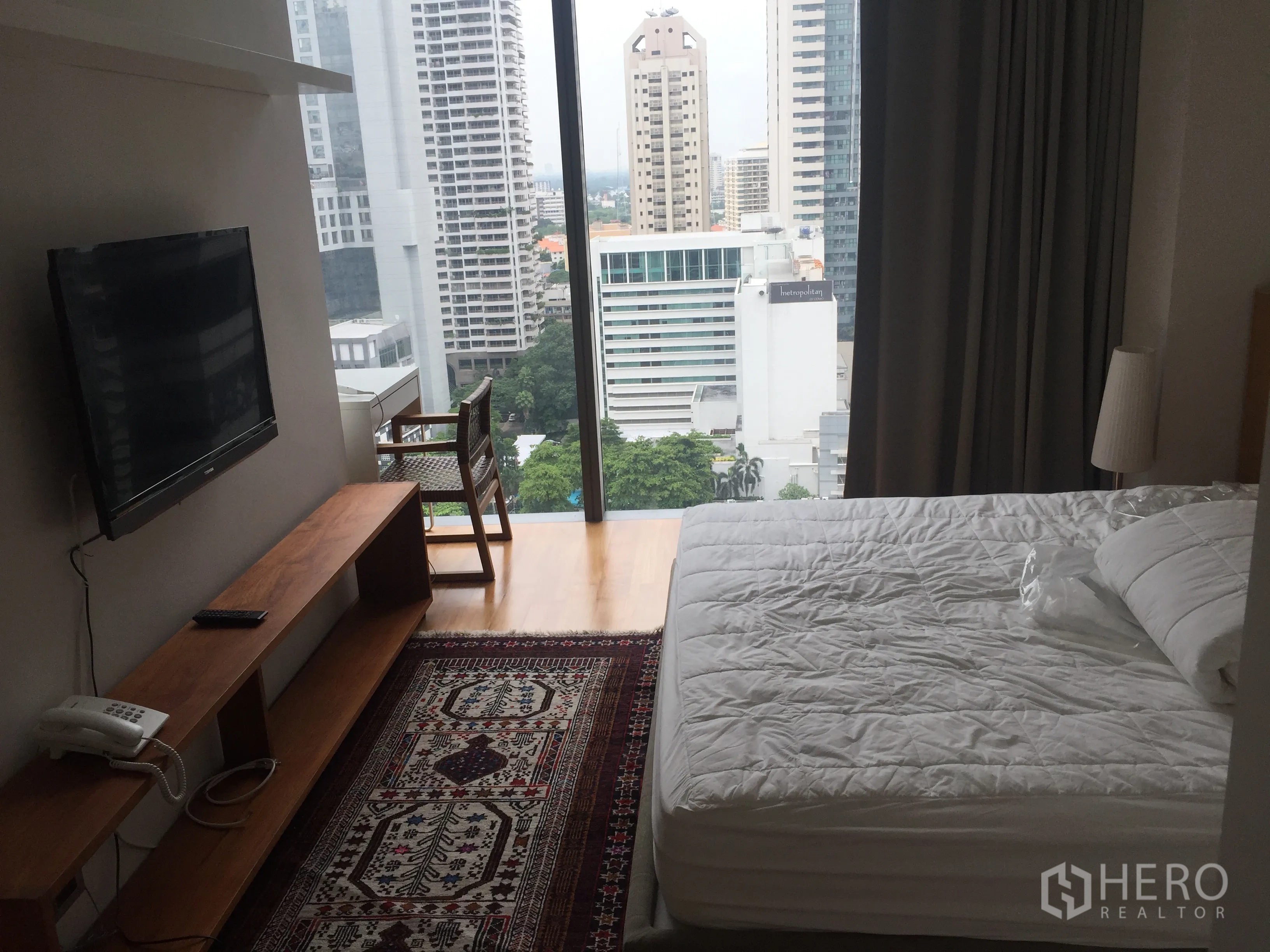 Condominium for rent in Bang Rak, Bangkok - Master bedroom with floor-to-ceiling window, city view, white bed and patterned rug.
