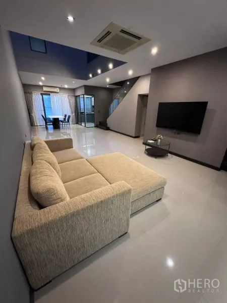 Townhouse for rent or sale in Lat Phrao, Bangkok - Open-plan living room with large sofa, TV wall and glossy floors.