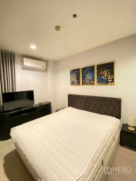 Condominium for rent in Khlong Toei, Bangkok - Cozy master bedroom with upholstered headboard, wall art, TV console and air conditioner in a Phra Khanong condo.