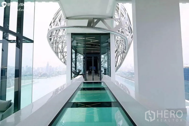 Condominium for rent in Watthana, Bangkok - Glass sky bridge above the pool leading to fitness facilities with skyline views.