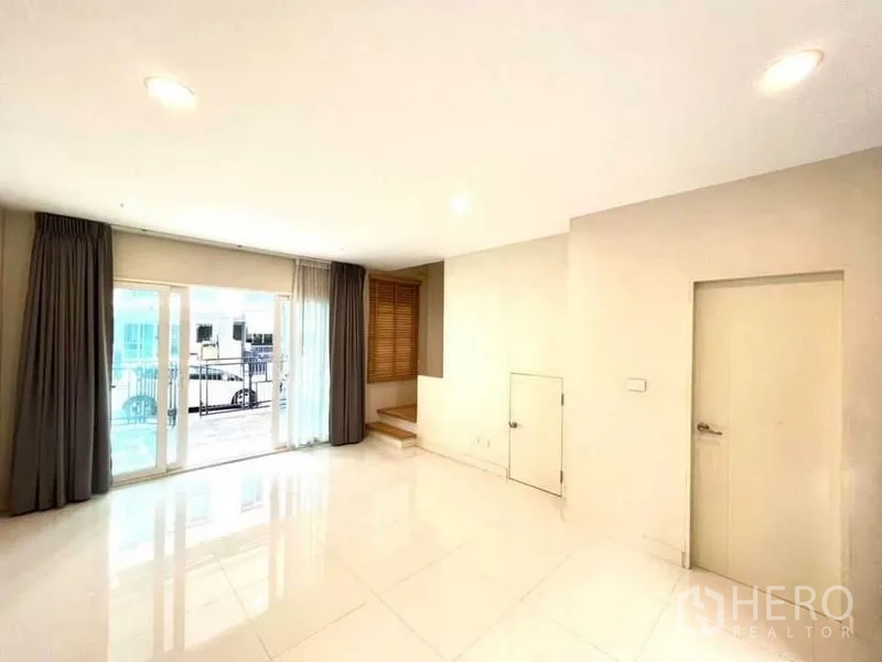 Townhouse for sale in Bang Kapi, Bangkok - Ground-floor living room with sliding doors to a terrace, under-stair storage, and drapes.