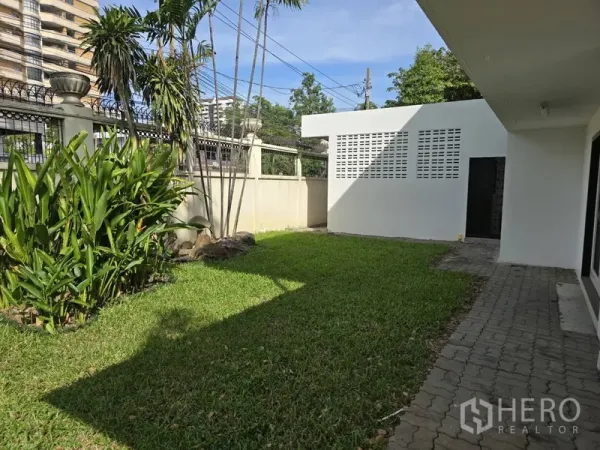 独立式住宅 出租在Watthana, Bangkok - 围墙内侧草坪与步道，棕榈树及白色杂物间。