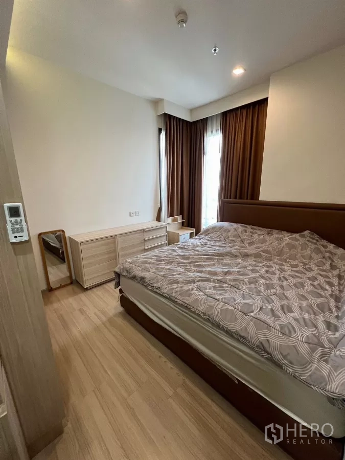Condominium for rent or sale in Chatuchak, Bangkok - Primary bedroom with double bed, dresser and tall windows with blackout curtains.