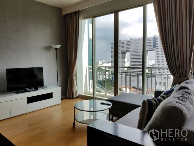 Condominium for rent in Chatuchak, Bangkok - Living room with sectional sofa, TV console and sliding doors to a balcony overlooking the city.
