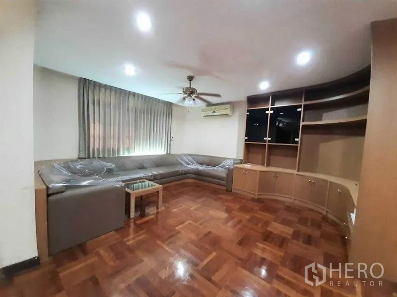 Detached House for rent in Watthana, Bangkok - Cozy family room with L‑shaped sofa, ceiling fan, and curved built‑in media shelves.