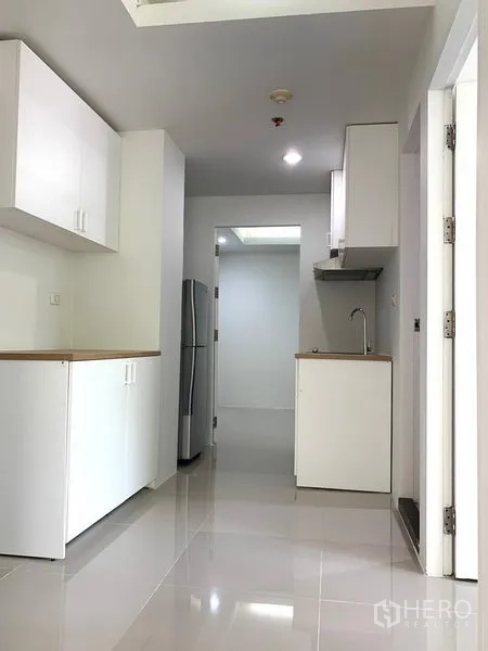 Condominium for rent or sale in Khlong Toei, Bangkok - Bright corridor kitchenette with white cabinets, wood countertops, glossy floor and a stainless fridge.