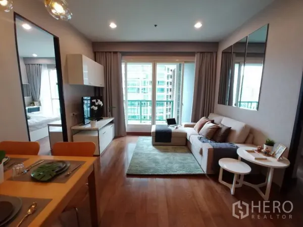 Condominium for rent in Pathum Wan, Bangkok - Bright living room with sofa, TV console, wood flooring and full-height balcony doors overlooking the city.