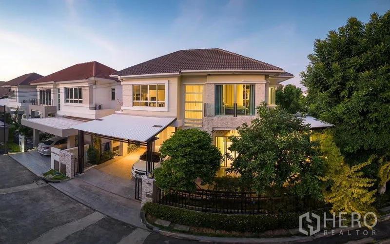 Detached House for rent or sale in Saphan Sung, Bangkok - Modern two‑storey detached house on a corner plot with double carport and warm exterior lighting in a quiet community.