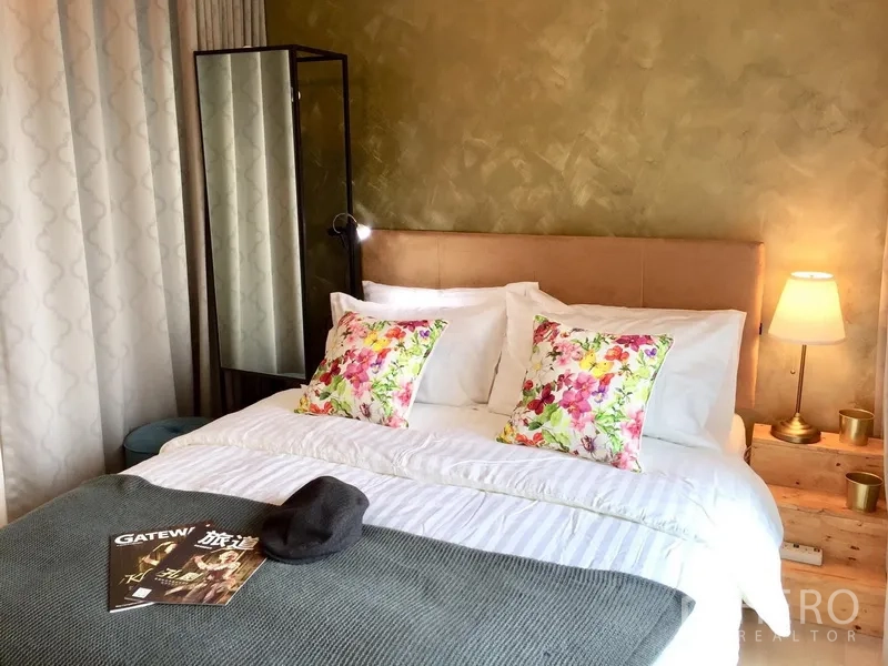 Condominium for rent in Khlong Toei, Bangkok - Second bedroom with floral pillows, bedside lamps and a freestanding mirror in soft lighting.