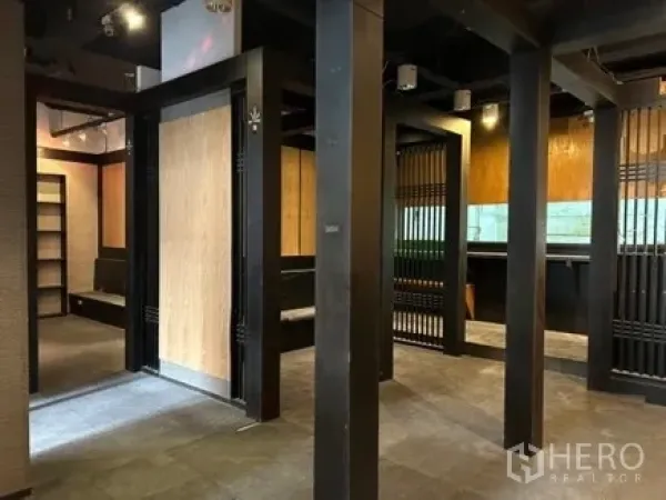 零售空间 出租在Bang Rak, Bangkok - 开放式零售室内，黑色立柱与木质格栅分隔，轨道灯与瓷砖地面。
