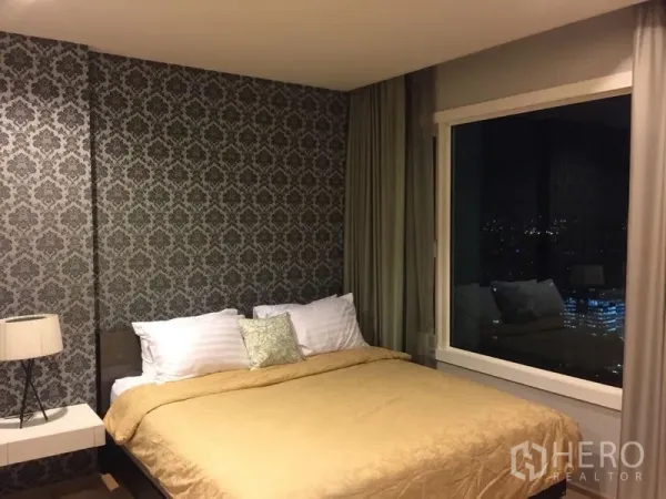 Condominium for rent in Khlong Toei, Bangkok - Bedroom with queen bed, feature wallpaper, large window with city night view, and curtains.