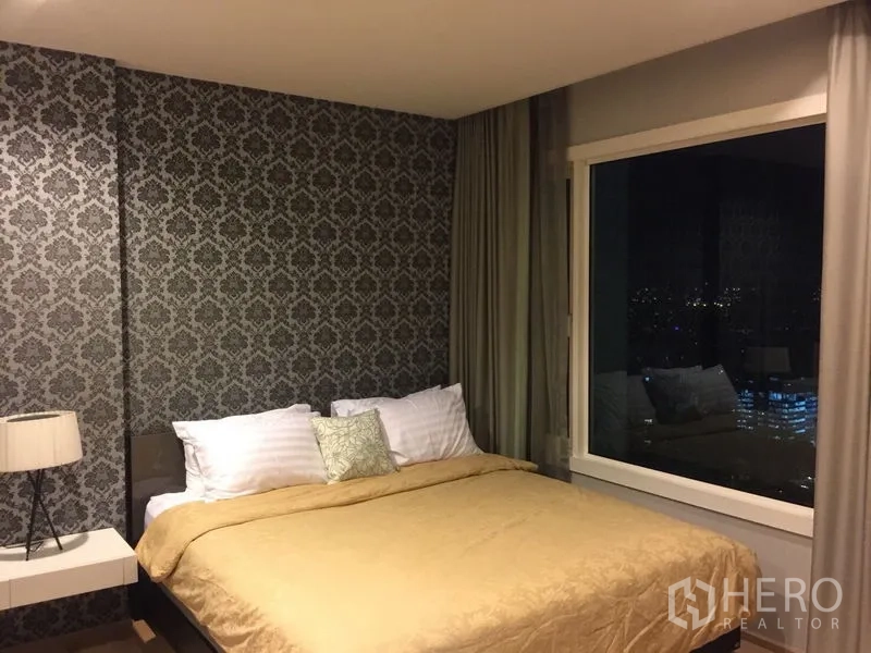 Condominium for rent in Khlong Toei, Bangkok - Bedroom with queen bed, feature wallpaper, large window with city night view, and curtains.