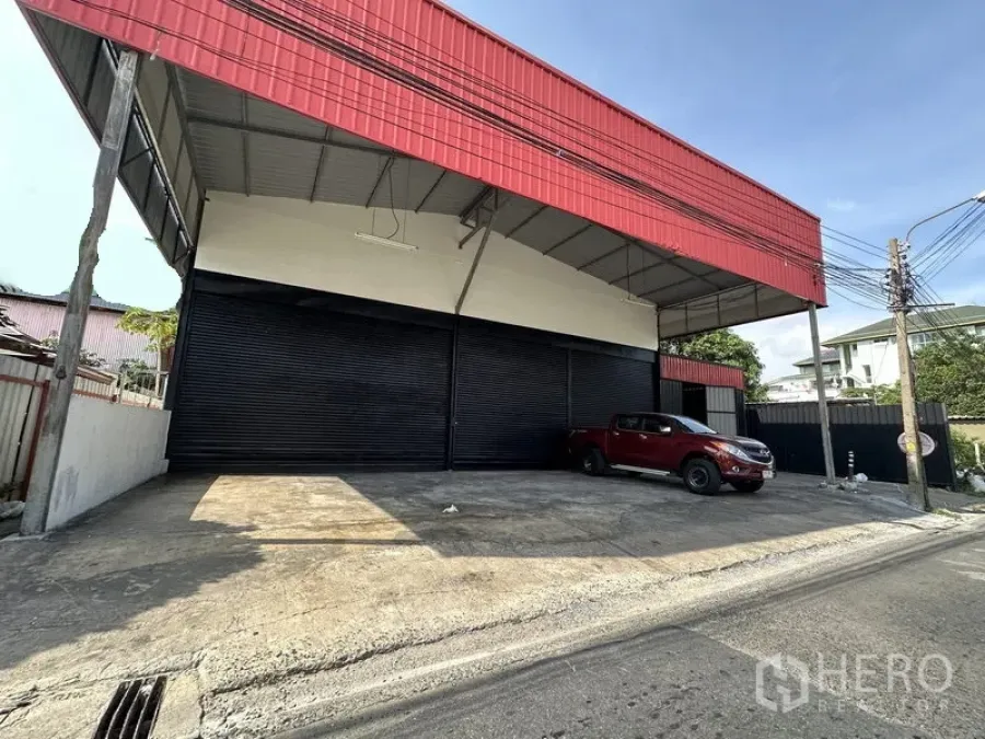 Warehouse for rent in Lat Phrao, Bangkok - Street view of Lat Phrao warehouse with red facade, wide covered loading bay and multiple black roller shutters.