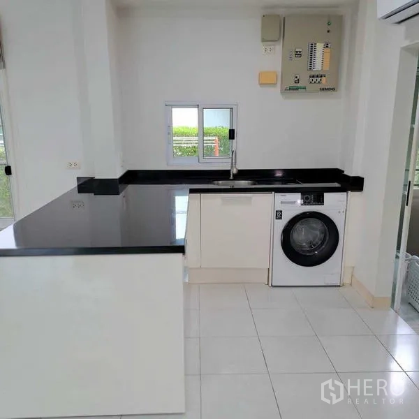 独立式住宅 出租在Prawet, Bangkok - 现代白色厨房，黑色石材台面、水槽与滚筒洗衣机。