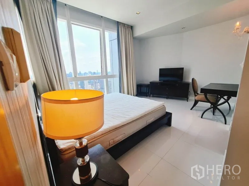 Condominium for rent in Khlong Toei, Bangkok - Bedroom corner with bedside lamp, large window and study desk overlooking the city.